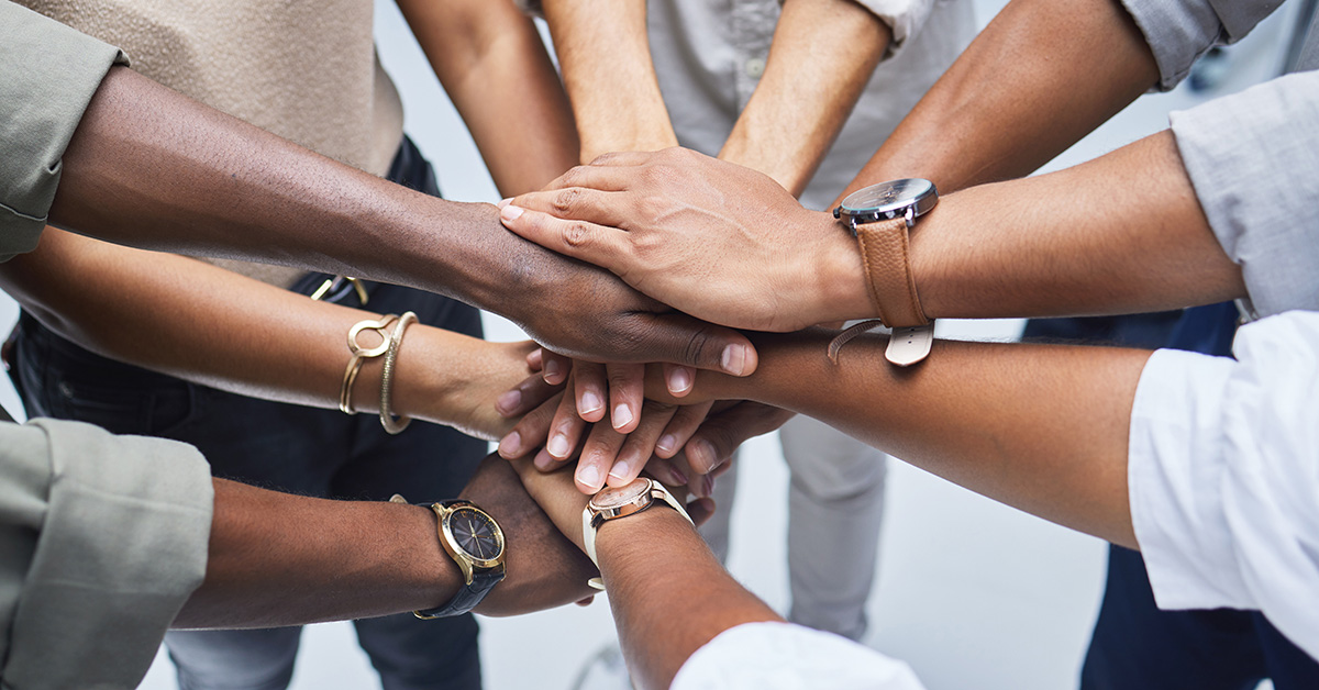 Several people all reaching to hold each other's hands in the center of the group.
