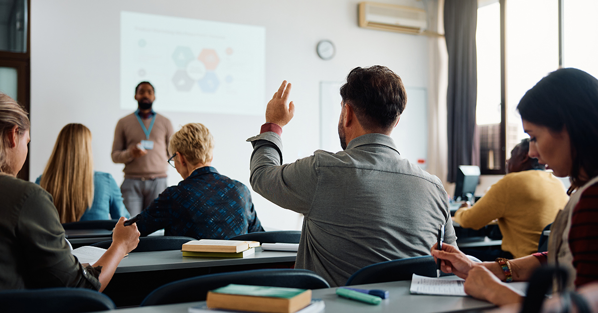 Man raises his hand in professional lecture setting.