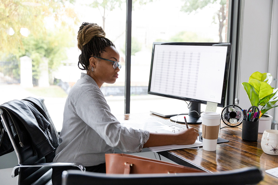Woman sits in front of a computer at a desk.