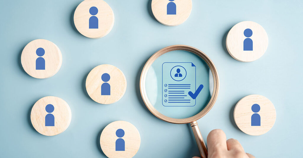 Hand holding magnifying glass over resume graphic, representing recruitment and HR hiring process