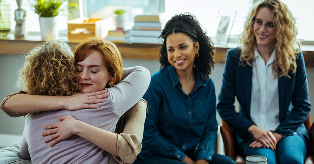two women hugging as two others look on supportively